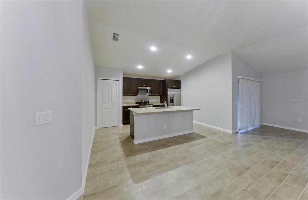 A kitchen with dark cabinets, a central island, and light tile flooring in an open space — 227 PENNFIELD STREET, LEHIGH ACRES, FL
