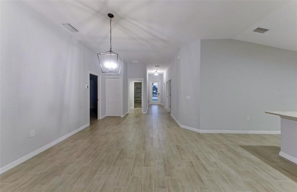 A hallway with light wood-look tile flooring leads toward a front door and entryway — 227 PENNFIELD STREET, LEHIGH ACRES, FL