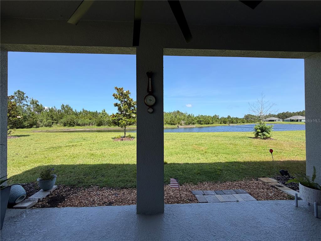 A covered patio overlooks a grassy lawn, a small pond, and a wooded area — 85 HUNTINGTON PLACE, ORMOND BEACH, FL