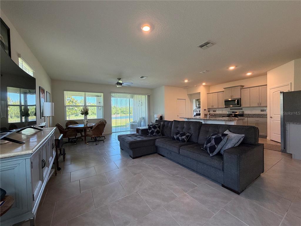 An open-concept living room and kitchen featuring tile flooring, a gray sectional, and sliding doors — 85 HUNTINGTON PLACE, ORMOND BEACH, FL