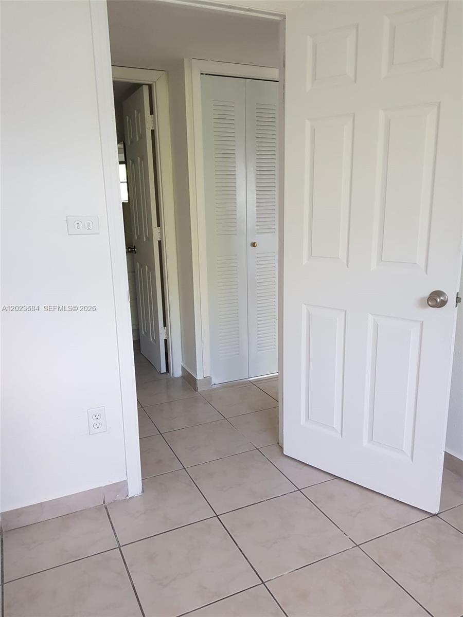 A tiled hallway features a white door, a louvered closet door, and a doorway beyond — 606 W 81st St # 314, Hialeah FL 33014, HIALEAH, FL