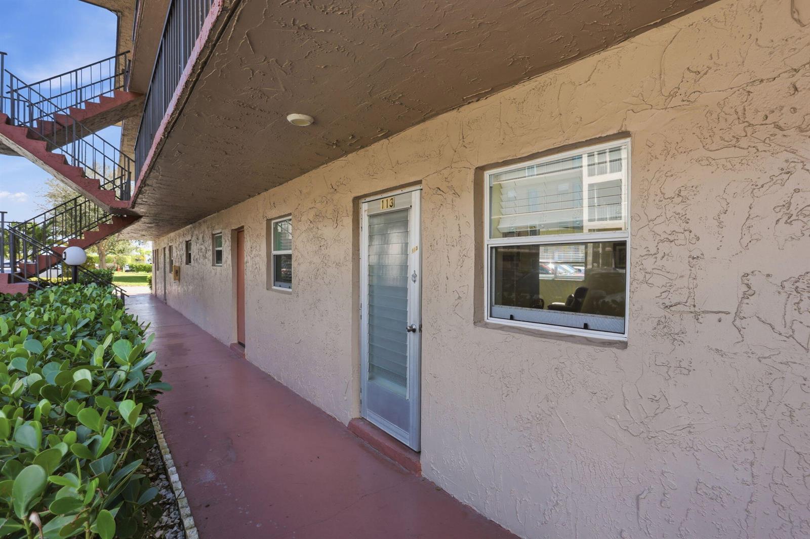 An exterior walkway leads to the entrance of apartment 113 with a window and stairs — 721 Lori Drive # 113, Palm Springs FL 33461, PALM SPRINGS, FL