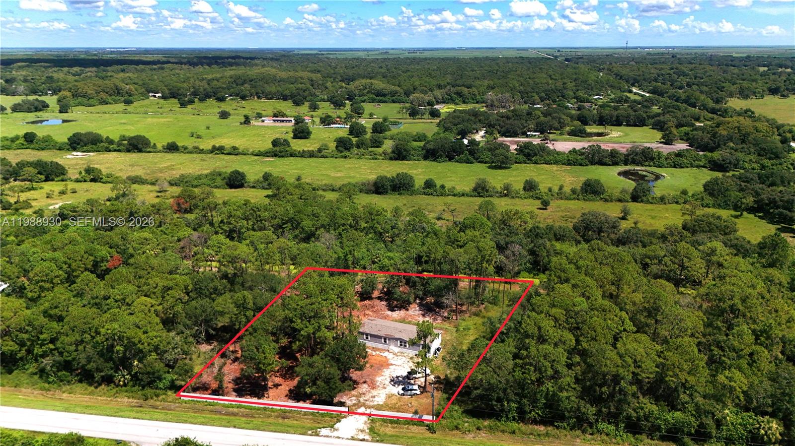 An aerial view shows a single-story house situated on a wooded lot with red boundary lines — 881 Woodland Blvd, Clewiston FL 33440, CLEWISTON, FL