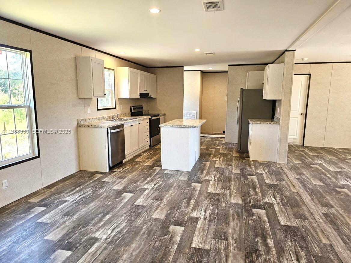 A kitchen features white cabinets, a central island, stainless steel appliances, and wood-look flooring — 881 Woodland Blvd, Clewiston FL 33440, CLEWISTON, FL