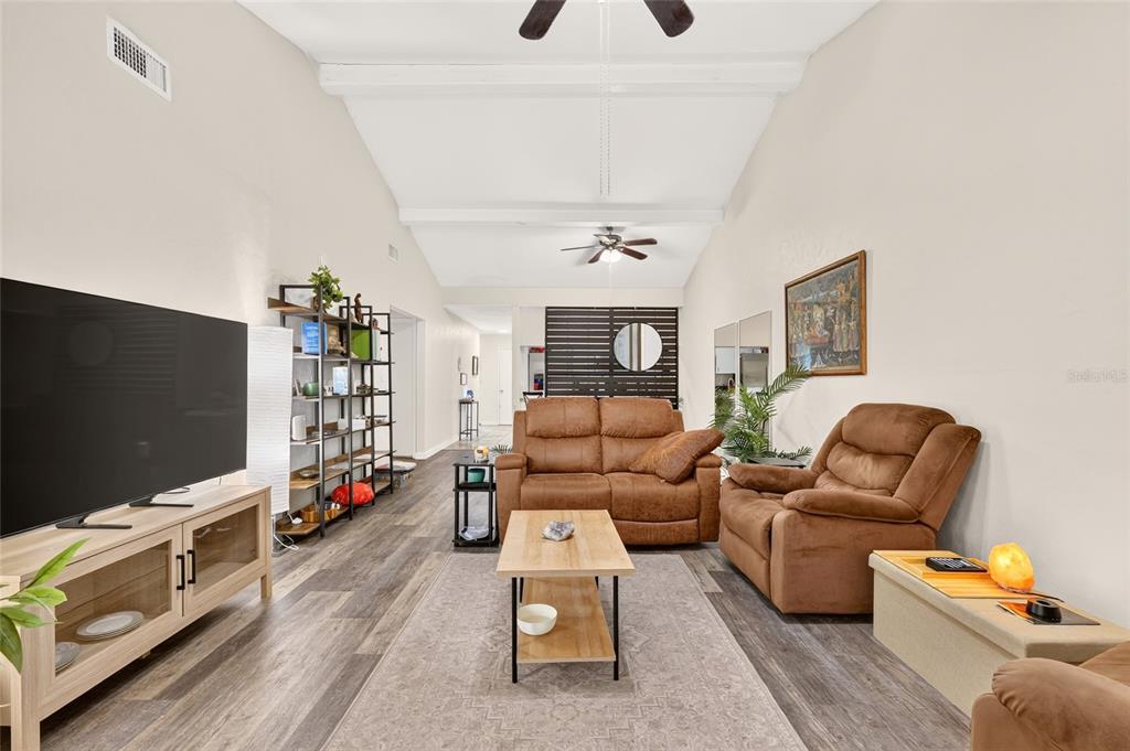 A living room features vaulted ceilings, wood-look flooring, brown furniture, and a large television — 11413 NW 67TH TERRACE, ALACHUA, FL
