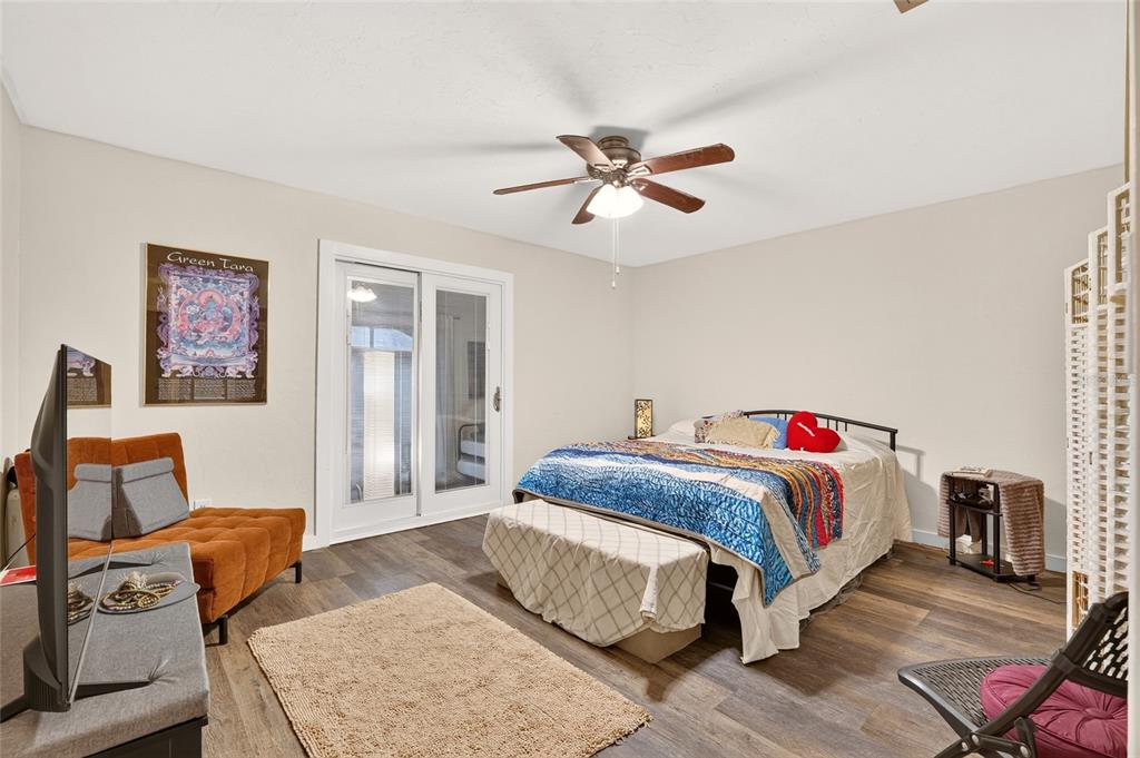 A bedroom features wood-look flooring, a ceiling fan, a bed, and sliding glass patio doors — 11413 NW 67TH TERRACE, ALACHUA, FL