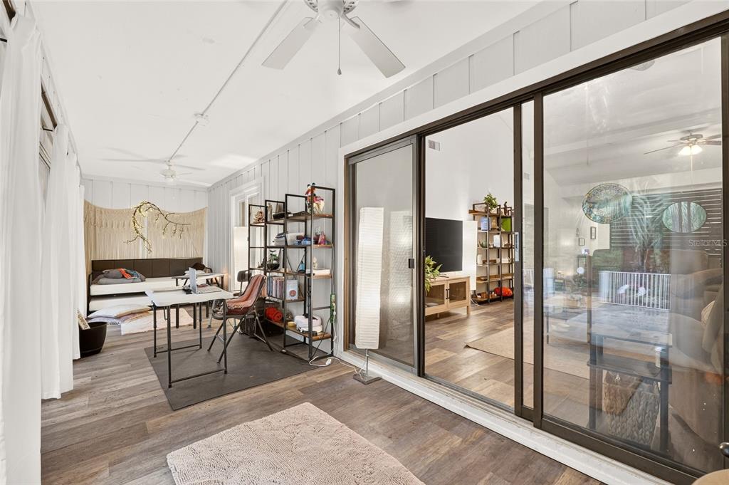 A sunroom with wood-look flooring, a desk, shelving, and sliding glass doors to the interior — 11413 NW 67TH TERRACE, ALACHUA, FL