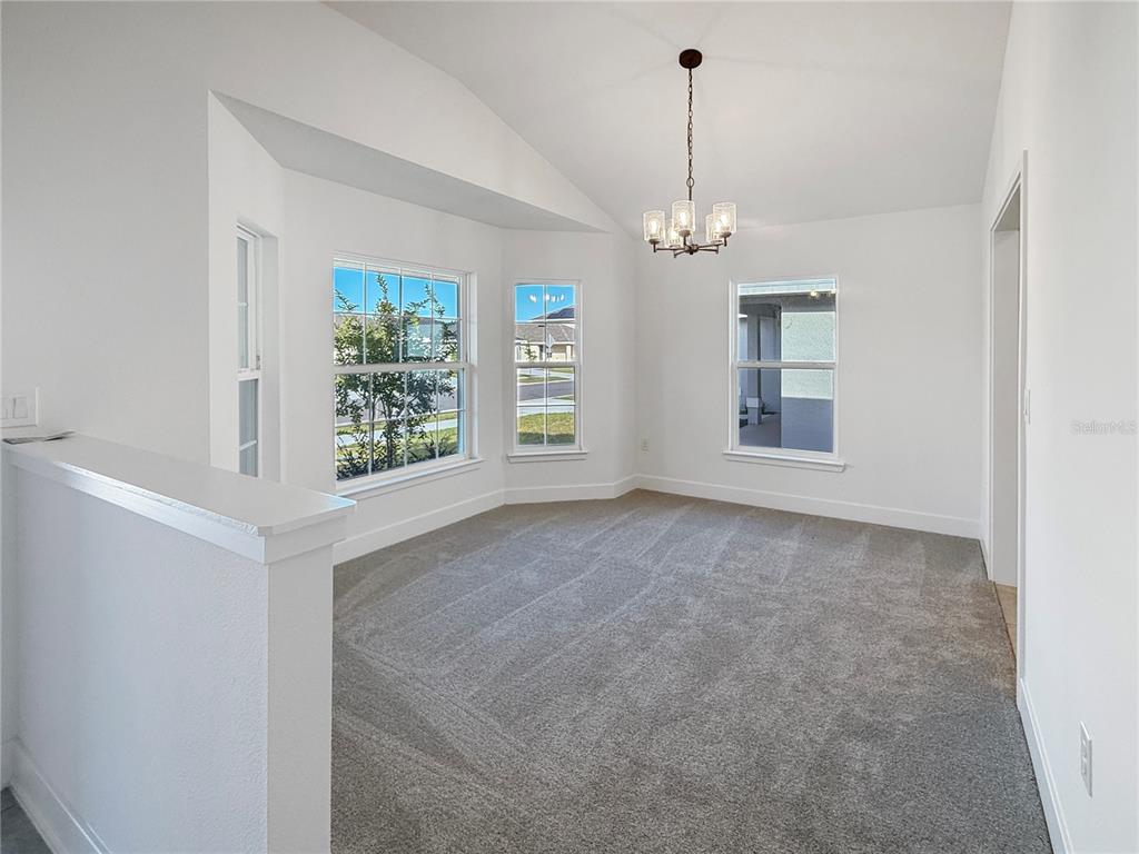 A bright dining room features gray carpeting, white walls, a vaulted ceiling, and a chandelier — 7584 BENT TREE LOOP, ST CLOUD, FL