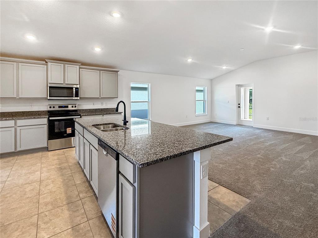 A kitchen with granite countertops and light gray cabinets opens to a carpeted living area — 7584 BENT TREE LOOP, ST CLOUD, FL