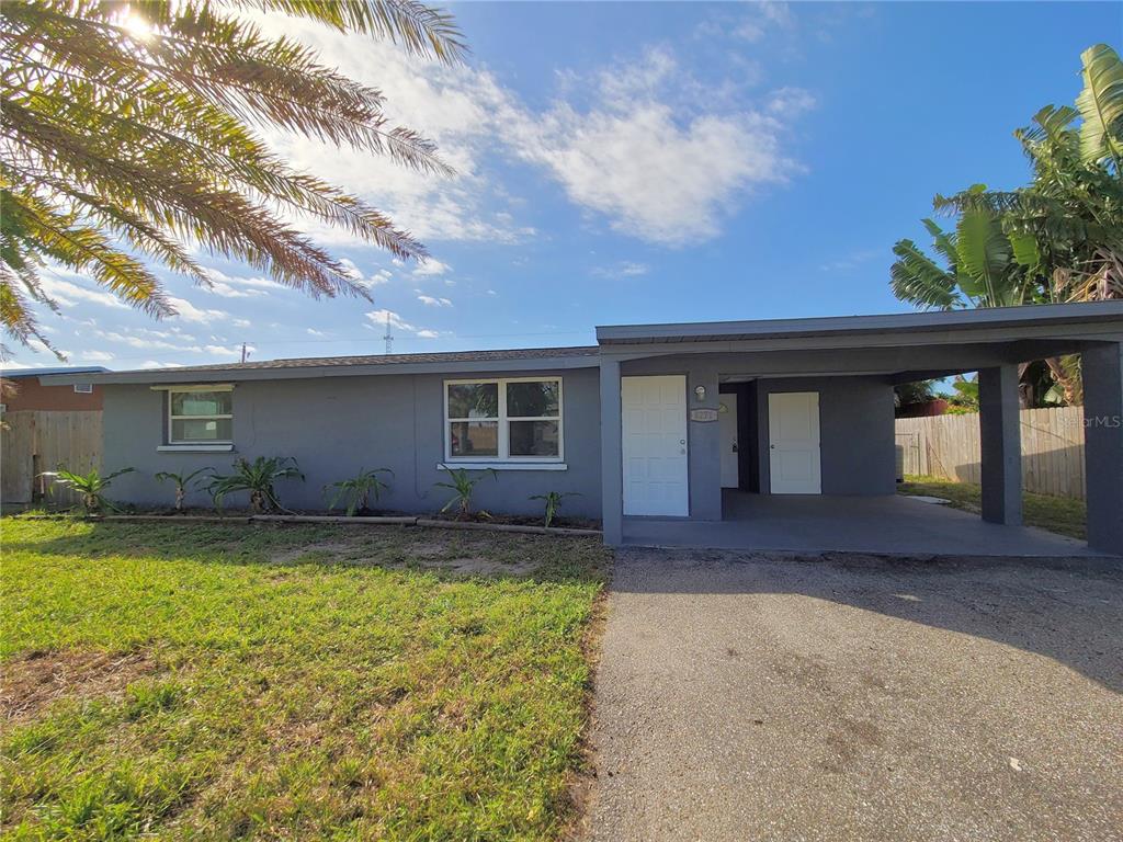 A single-story gray house features a front carport, a concrete driveway, and a grassy lawn — 8271 PELICAN ROAD, ENGLEWOOD, FL