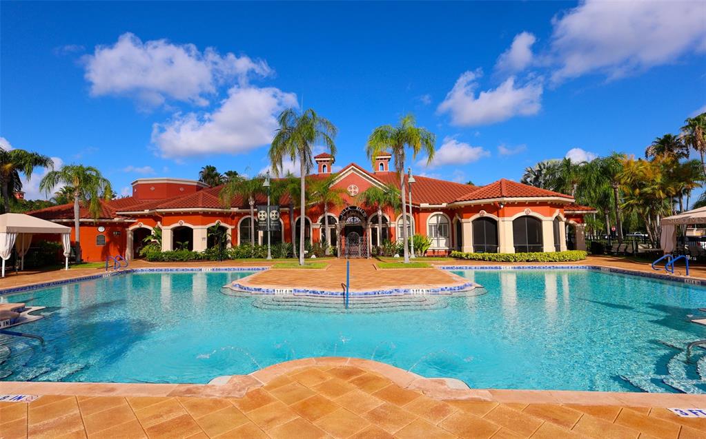 A swimming pool sits in front of a large, orange-colored clubhouse with a tiled roof — 2731 VIA CAPRI UNIT 937, CLEARWATER, FL