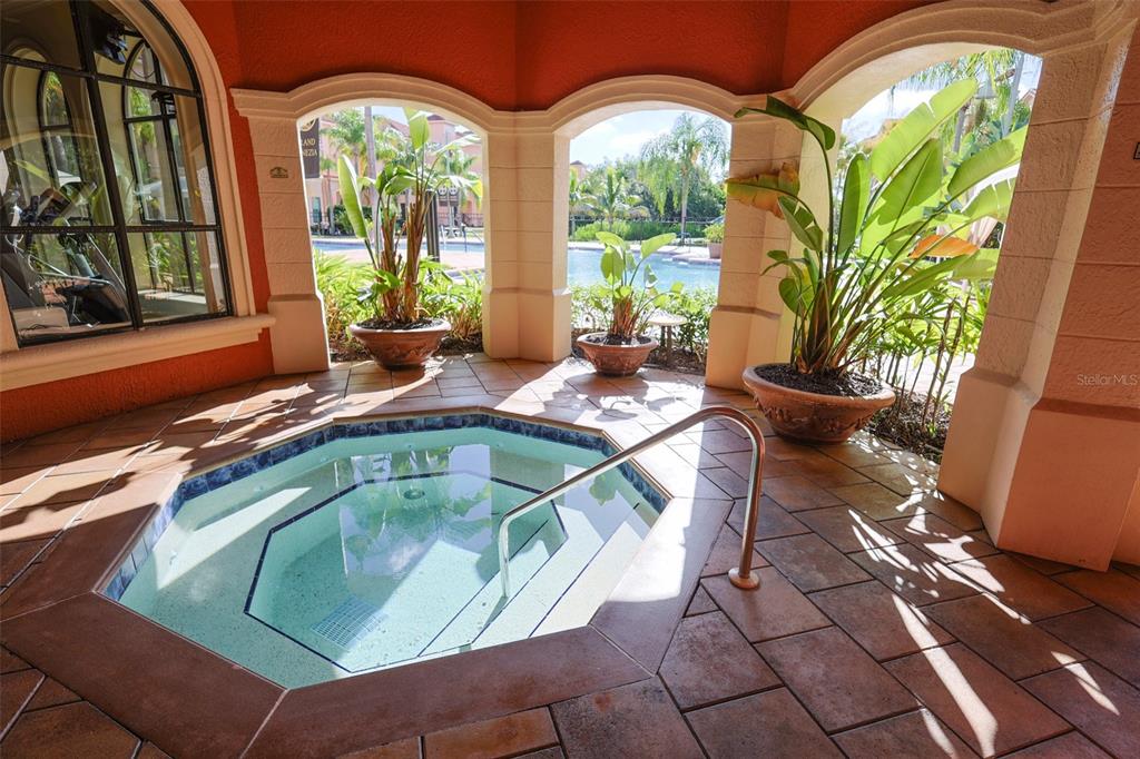 A covered outdoor hot tub sits on a tiled patio overlooking a swimming pool area — 2731 VIA CAPRI UNIT 937, CLEARWATER, FL