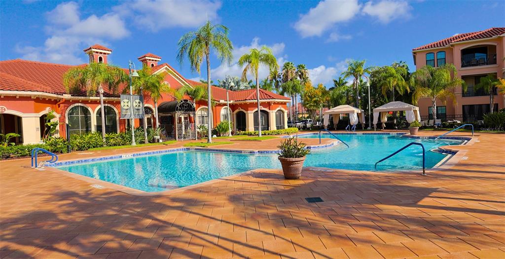 A swimming pool with blue tiles sits in front of a Mediterranean-style clubhouse and building — 2731 VIA CAPRI UNIT 937, CLEARWATER, FL