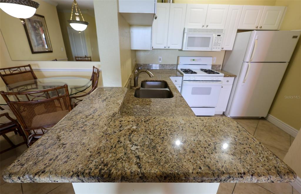 A kitchen features granite countertops, white cabinetry, a white stove, and a white refrigerator — 2731 VIA CAPRI UNIT 937, CLEARWATER, FL