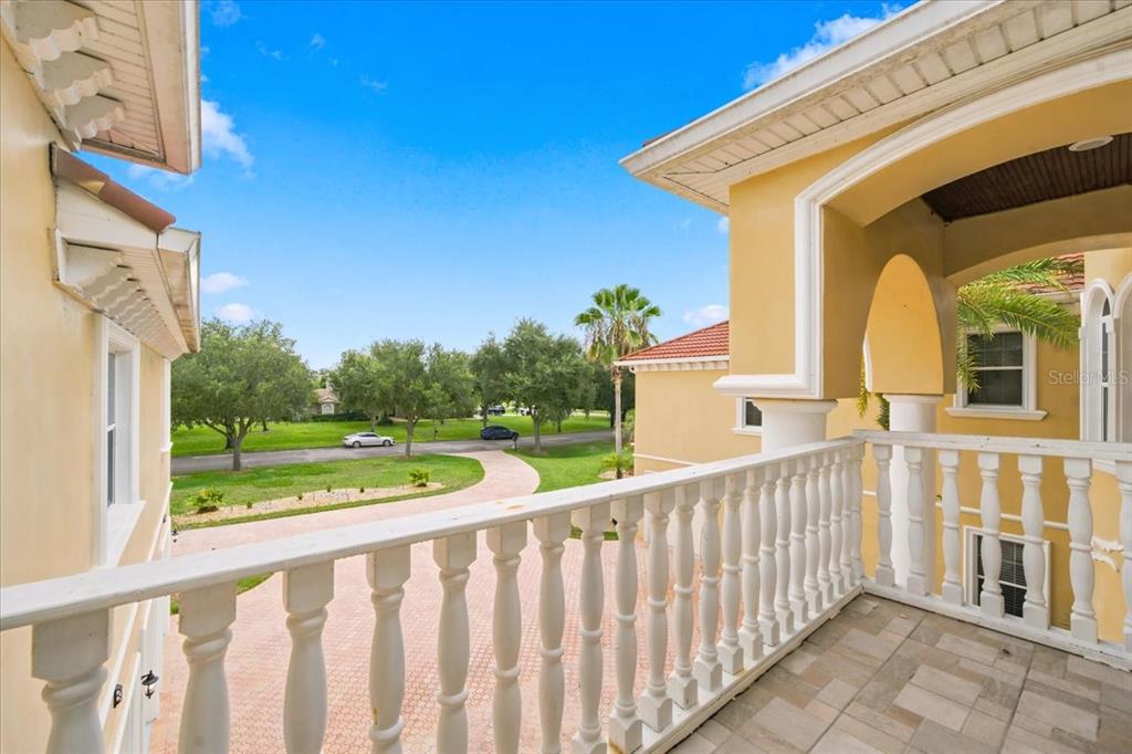 A second-story balcony with white balustrades overlooks a paved driveway and a grassy neighborhood street — 19402 JACOBS RIVER RUN, LUTZ, FL