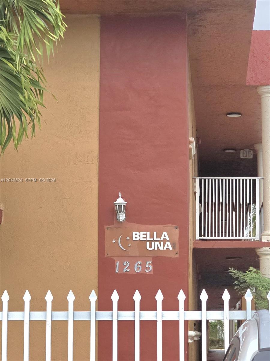 The exterior of a building features a sign reading Bella Una 1265 and a white fence — 1265 W 24th St # 201, Hialeah FL 33010, HIALEAH, FL