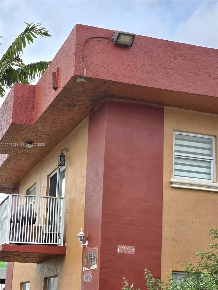 The exterior of a two-story building features red and tan stucco walls and a balcony — 1265 W 24th St # 201, Hialeah FL 33010, HIALEAH, FL