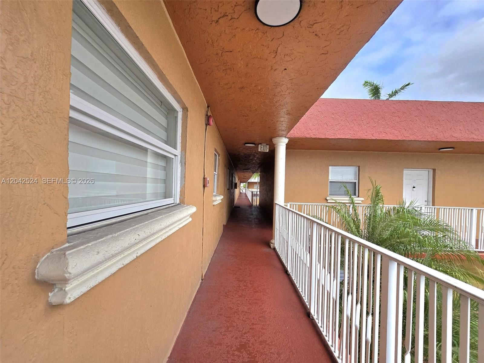 An outdoor walkway with a red floor, white railings, and tan stucco walls — 1265 W 24th St # 201, Hialeah FL 33010, HIALEAH, FL