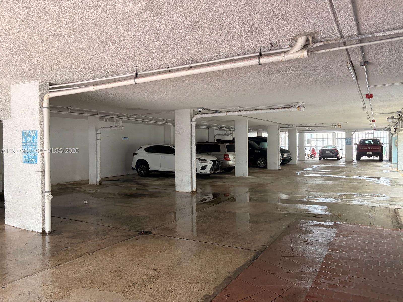 A covered parking garage features concrete pillars, overhead pipes, and several parked vehicles — 335 Collins Ave # 302, Miami Beach FL 33139, MIAMI BEACH, FL