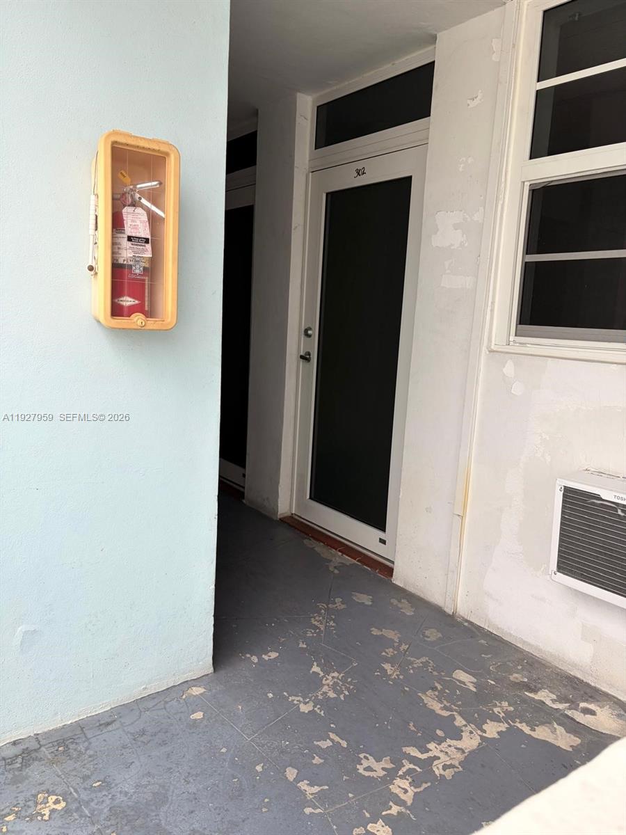 A fire extinguisher in a wall-mounted cabinet sits beside a door labeled 302 — 335 Collins Ave # 302, Miami Beach FL 33139, MIAMI BEACH, FL