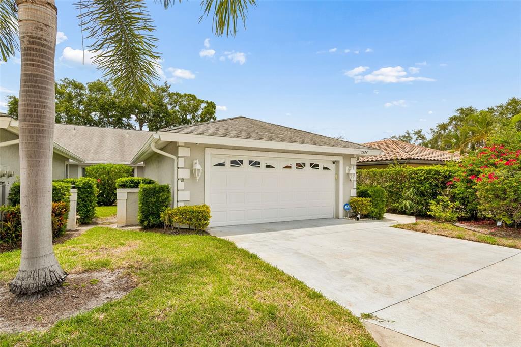 A single-story house exterior features a white two-car garage, a concrete driveway, and landscaping — 7656 PALM AIRE LANE, SARASOTA, FL