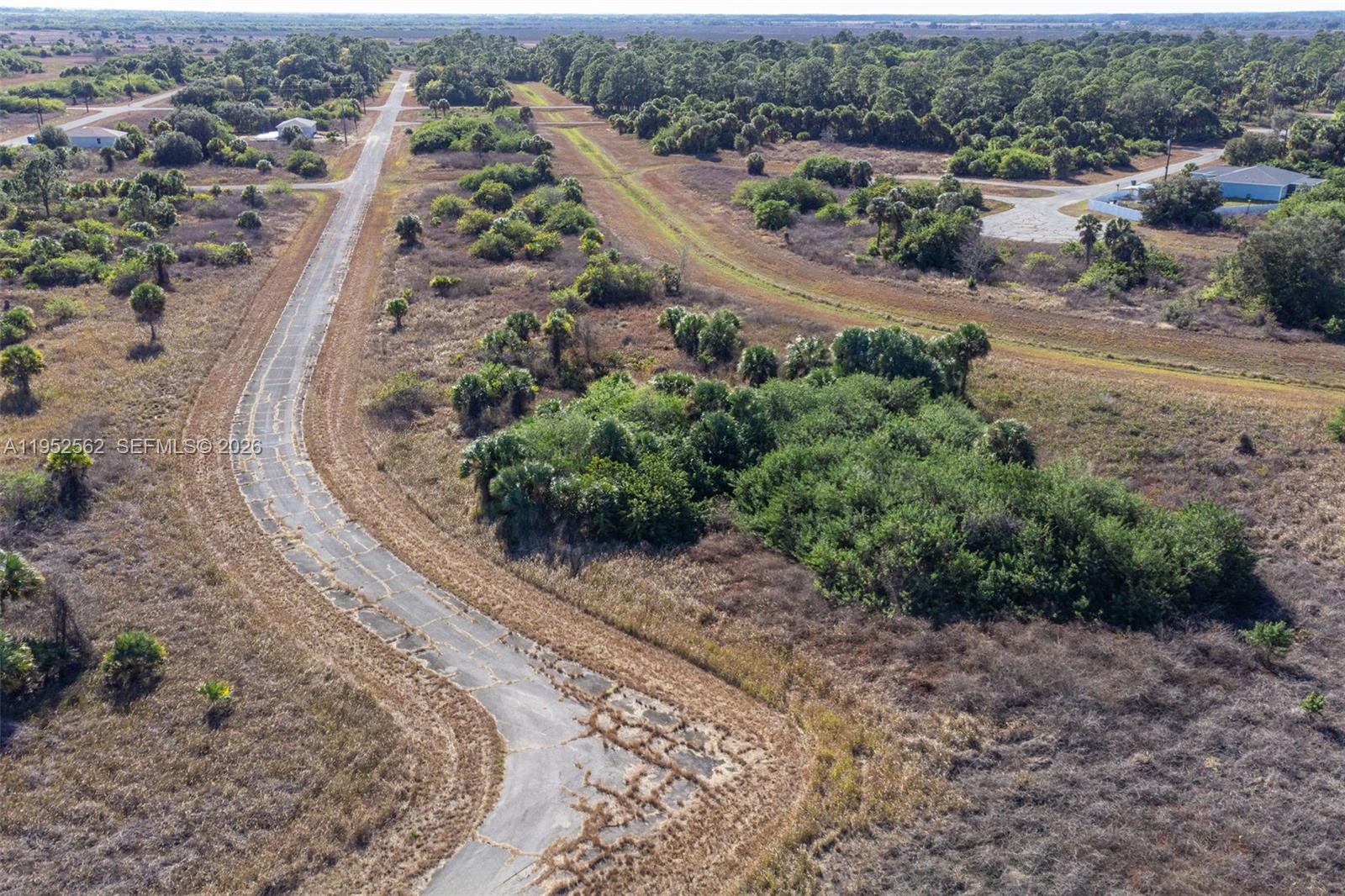 An aerial view shows a winding, weathered road surrounded by undeveloped, brush-covered land and trees — 403 Boca Cir, La Belle FL 33935, LA BELLE, FL