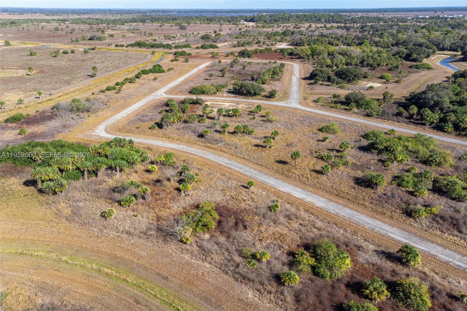 An aerial view shows a paved road winding through a large, undeveloped, grassy field — 403 Boca Cir, La Belle FL 33935, LA BELLE, FL
