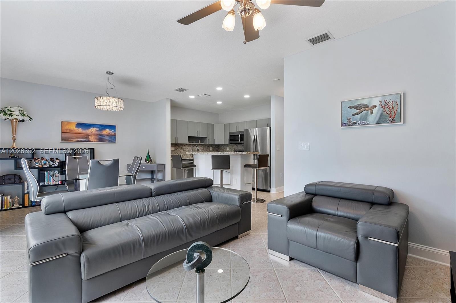 A living room with gray leather furniture, a glass coffee table, and an open kitchen — 12941 SW 29th St, Miramar FL 33027, MIRAMAR, FL