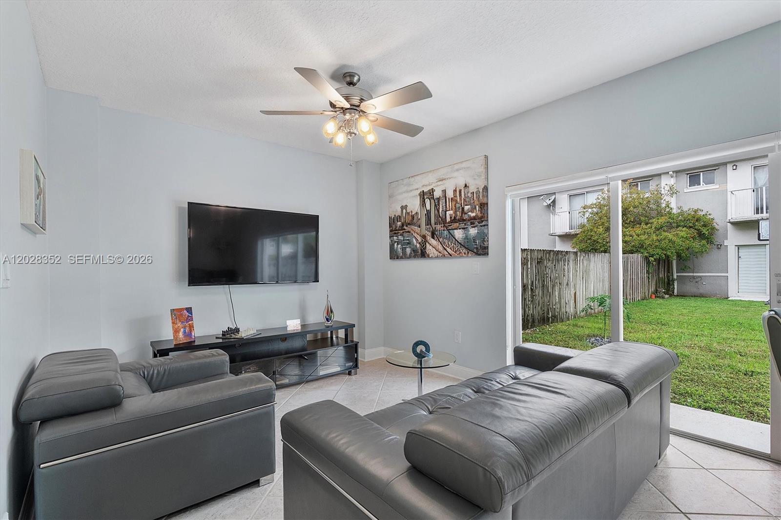 A living room features gray leather furniture, a wall-mounted television, and a sliding glass door — 12941 SW 29th St, Miramar FL 33027, MIRAMAR, FL