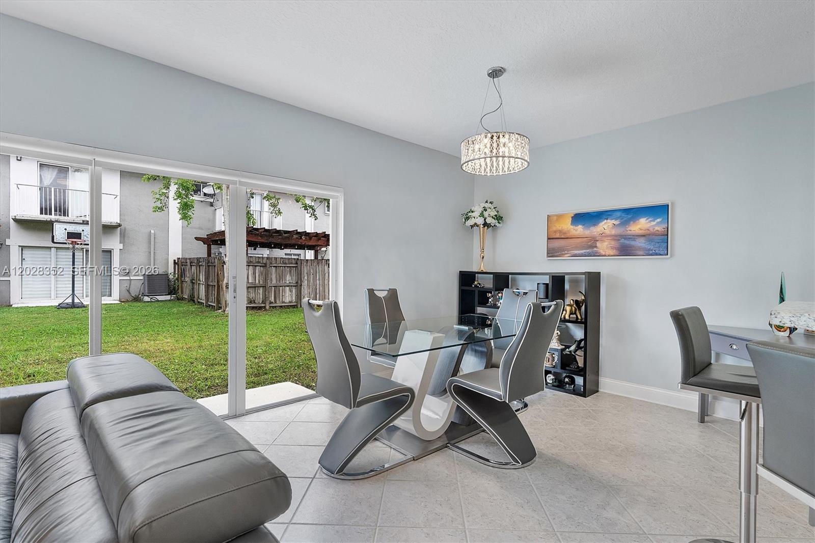 A dining room features a glass table, modern chairs, a chandelier, and a sliding door — 12941 SW 29th St, Miramar FL 33027, MIRAMAR, FL