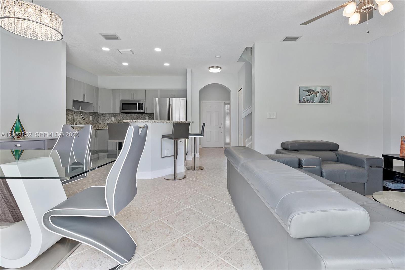An open-concept living and dining area features gray furniture, tile flooring, and a kitchen — 12941 SW 29th St, Miramar FL 33027, MIRAMAR, FL