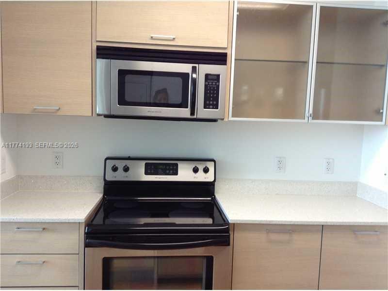 A kitchen features light wood cabinets, a stainless steel microwave, and a black electric range — 350 NE 24th St # 1108, Miami FL 33137, MIAMI, FL