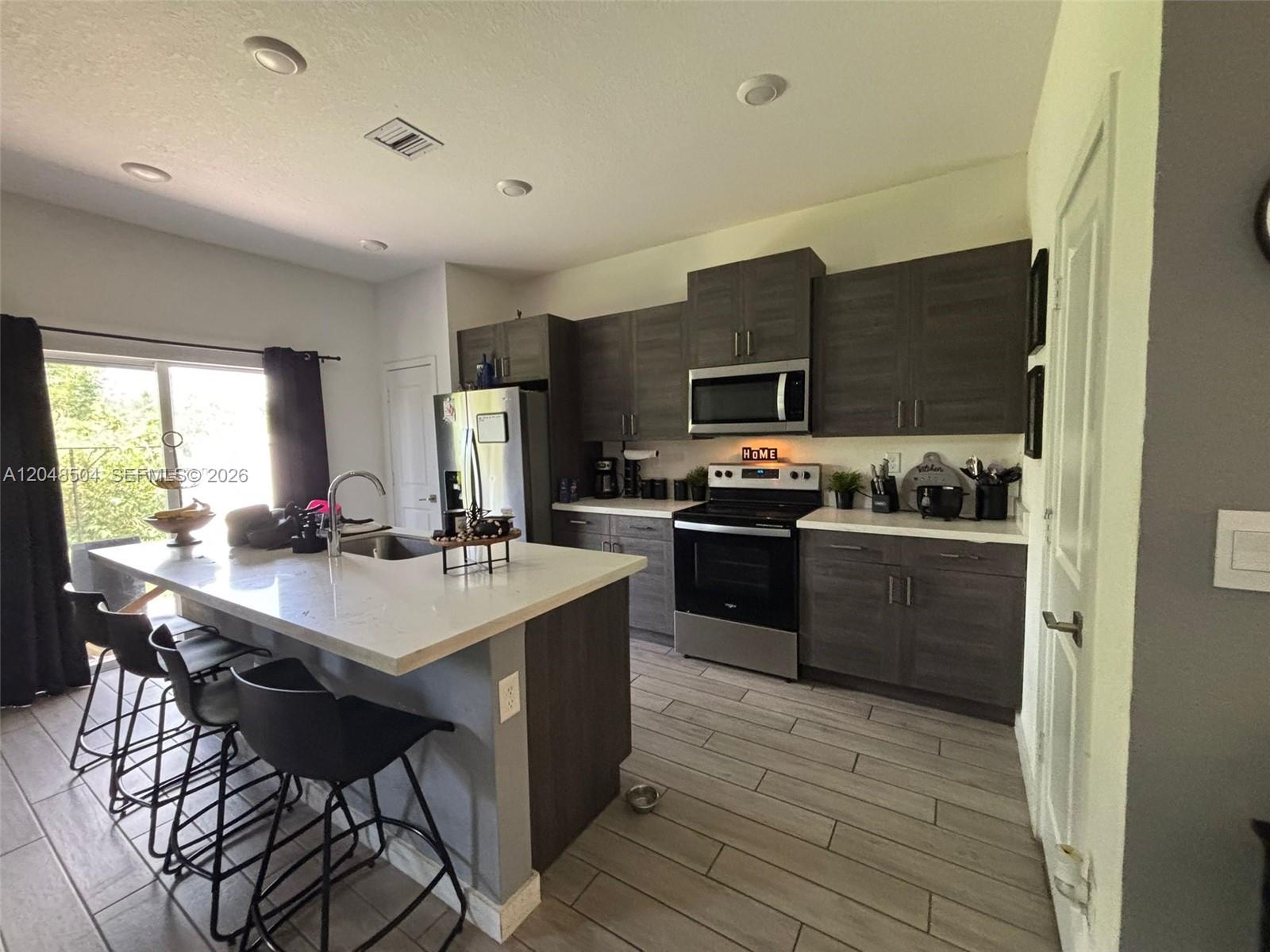 A modern kitchen features dark wood cabinetry, white countertops, and a central island with seating — 830 SE 19th St, Homestead FL 33034, HOMESTEAD, FL