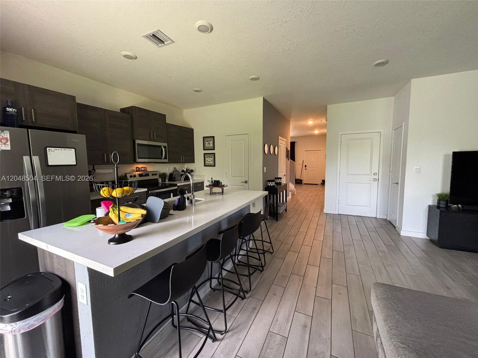 A modern kitchen features dark cabinetry, a white quartz island, and light wood-look tile flooring — 830 SE 19th St, Homestead FL 33034, HOMESTEAD, FL