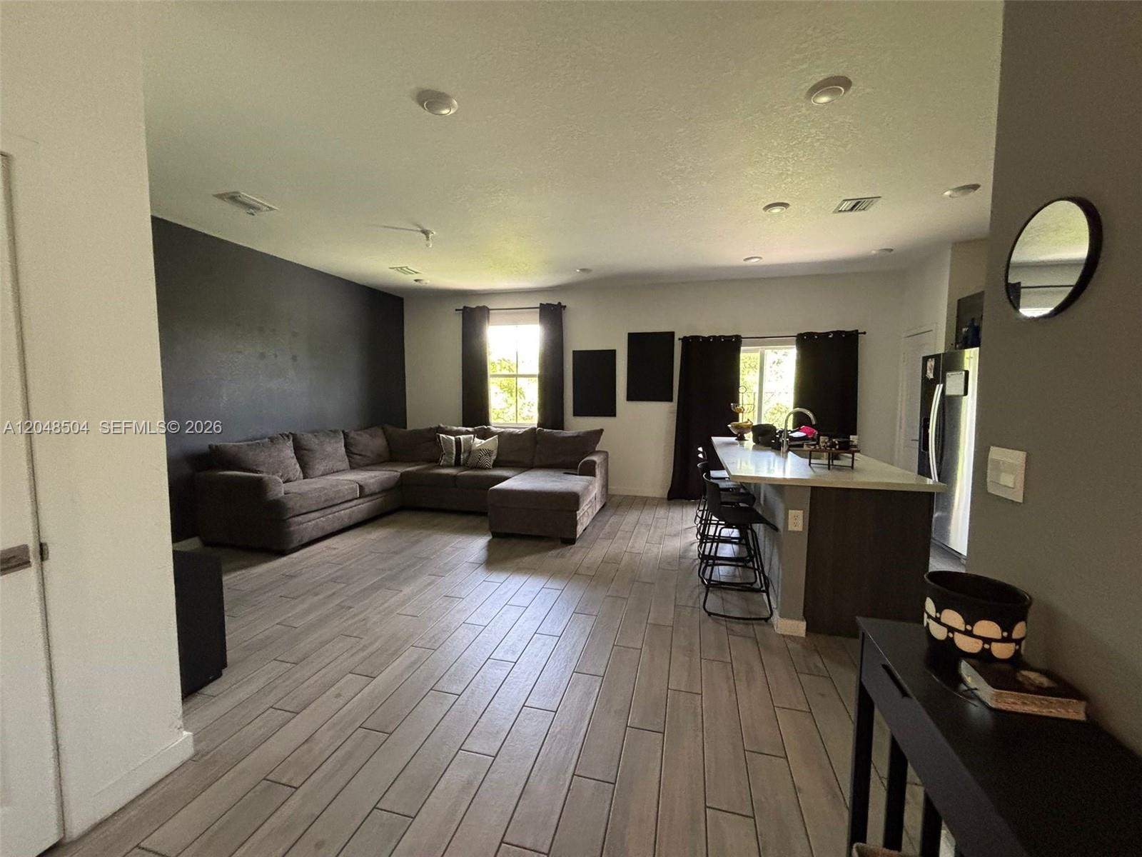 An open-concept living room features a dark accent wall, sectional sofa, and kitchen island — 830 SE 19th St, Homestead FL 33034, HOMESTEAD, FL