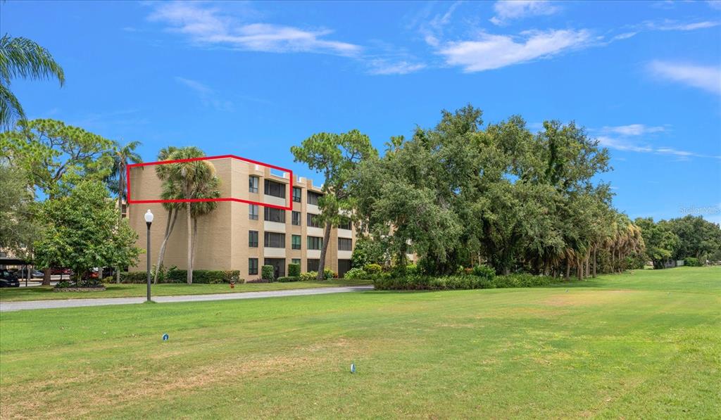 A multi-story tan apartment building is surrounded by green lawns and mature trees — 2614 COVE CAY DRIVE UNIT 409, CLEARWATER, FL