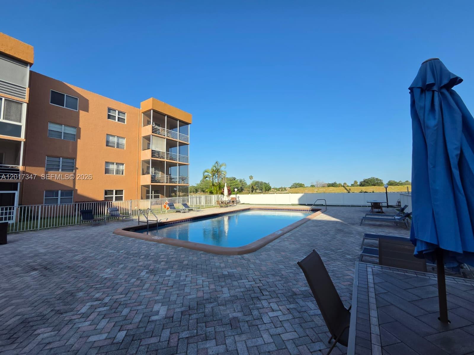 An outdoor swimming pool is surrounded by a brick patio and a multi-story apartment building — 3050 E Sunrise Lakes Dr # 402, Sunrise FL 33322, SUNRISE, FL