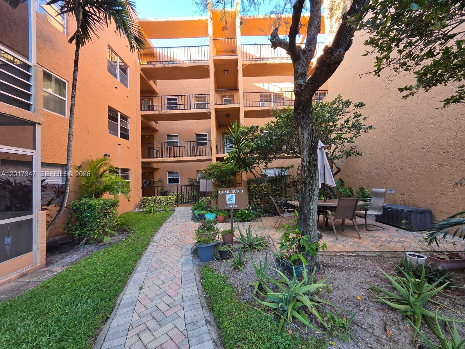 A brick walkway leads to a courtyard with a sign for Quail Run II Plaza — 3050 E Sunrise Lakes Dr # 402, Sunrise FL 33322, SUNRISE, FL