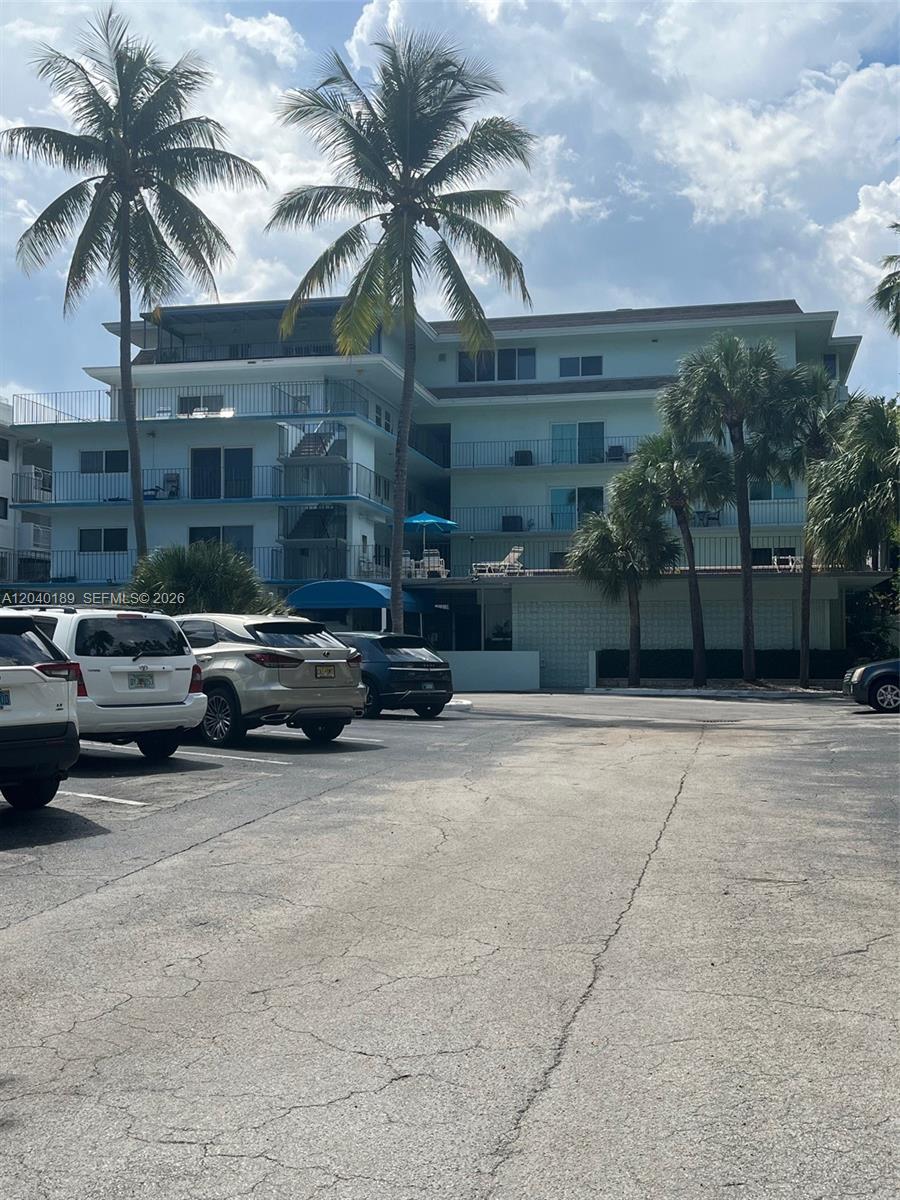 A multi-story apartment building with balconies stands behind a paved parking lot with cars — 2539 S Bayshore Dr # 320A, Miami FL 33133, MIAMI, FL