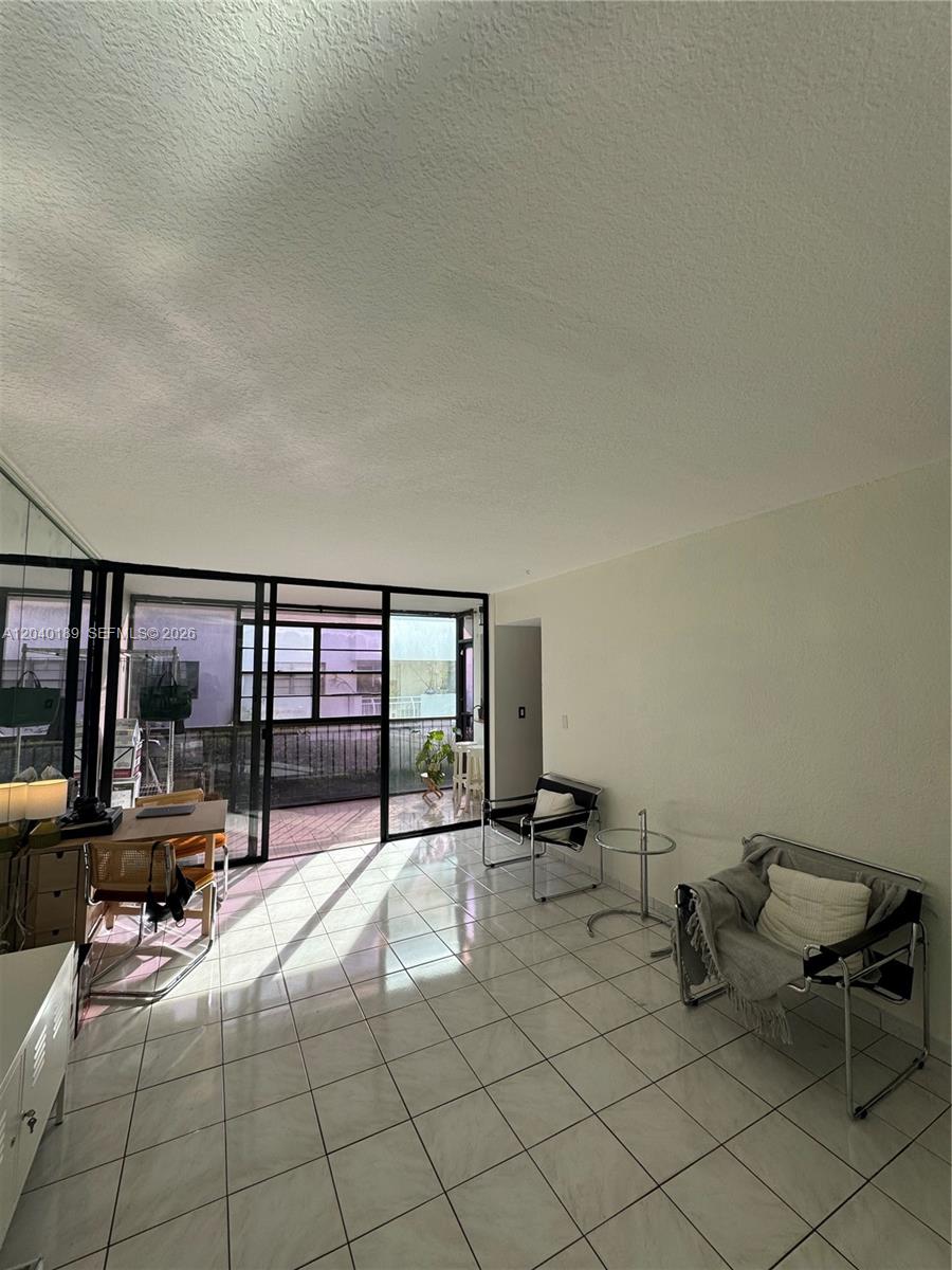 A living room with white tile floors, a glass-walled balcony, and two modern metal chairs — 2539 S Bayshore Dr # 320A, Miami FL 33133, MIAMI, FL