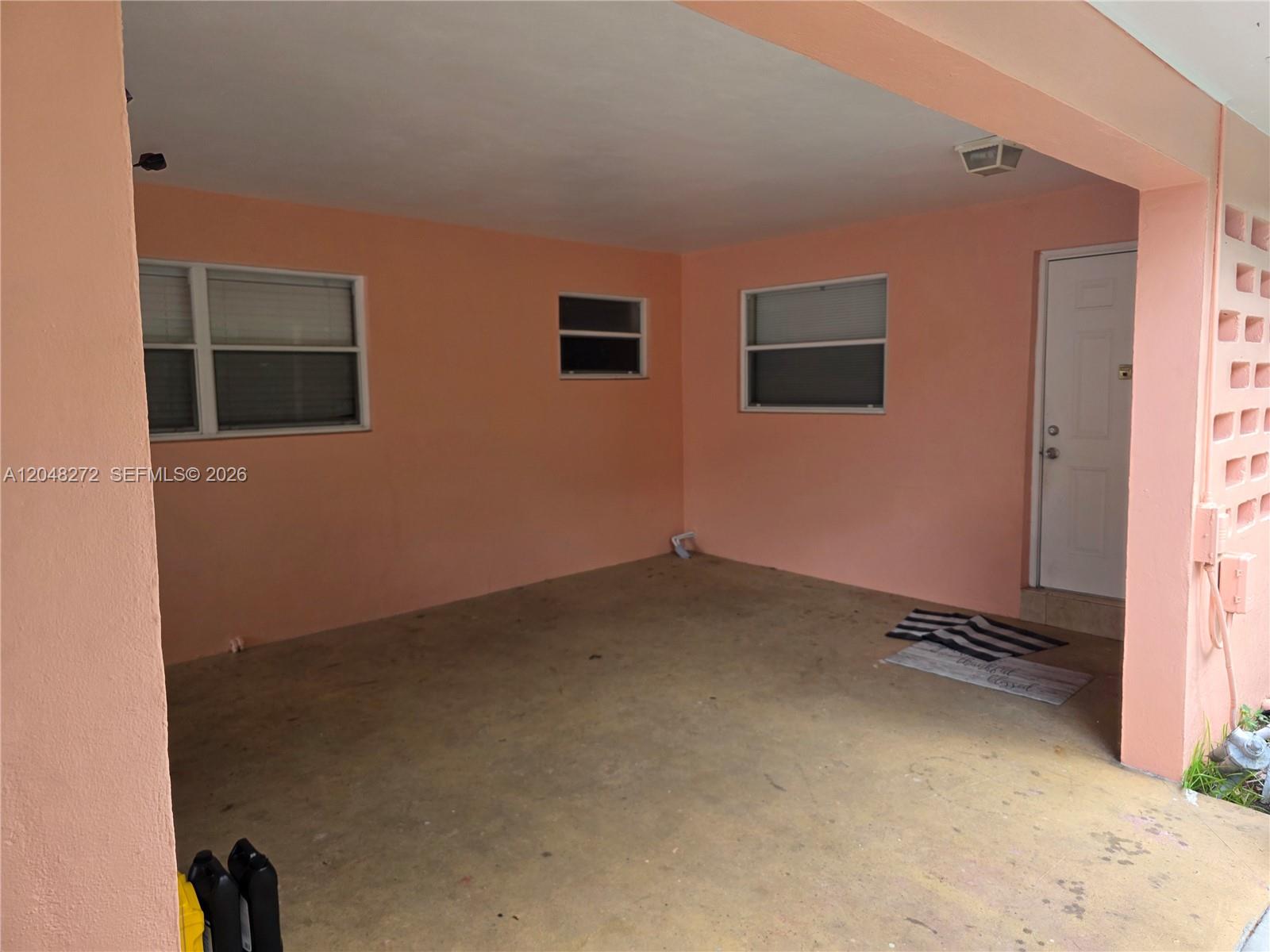 A covered outdoor patio with peach-colored walls, concrete flooring, and a white entry door — 6130 Funston St, Hollywood FL 33023, HOLLYWOOD, FL