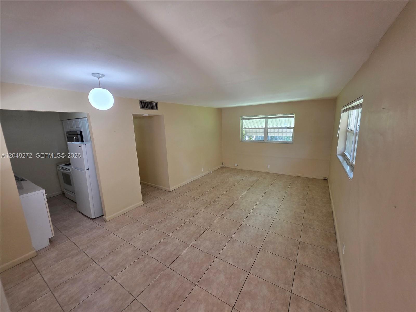 An empty room with beige tile flooring, light-colored walls, and an adjacent kitchen area — 6130 Funston St, Hollywood FL 33023, HOLLYWOOD, FL
