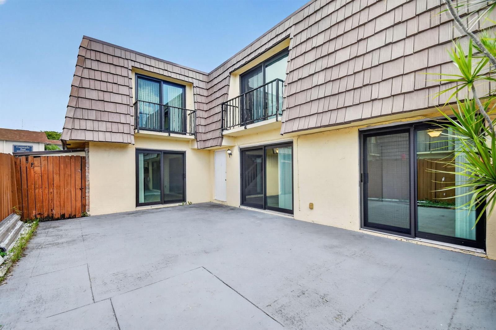 A two-story building exterior features a concrete patio, sliding glass doors, and upper-level balconies — 744 Springdale Circle, Palm Springs FL 33461, PALM SPRINGS, FL