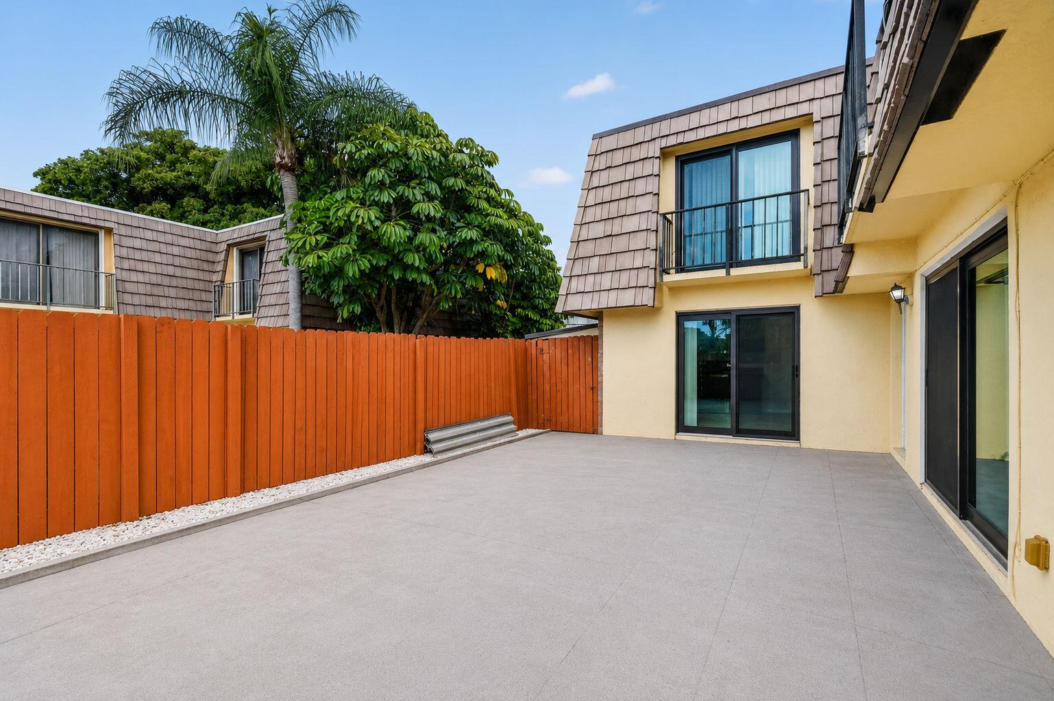A paved patio area sits beside a yellow building with sliding glass doors and fencing — 744 Springdale Circle, Palm Springs FL 33461, PALM SPRINGS, FL
