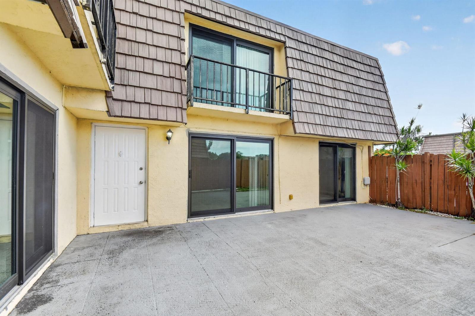 A two-story building exterior features a concrete patio, sliding glass doors, and a balcony — 744 Springdale Circle, Palm Springs FL 33461, PALM SPRINGS, FL