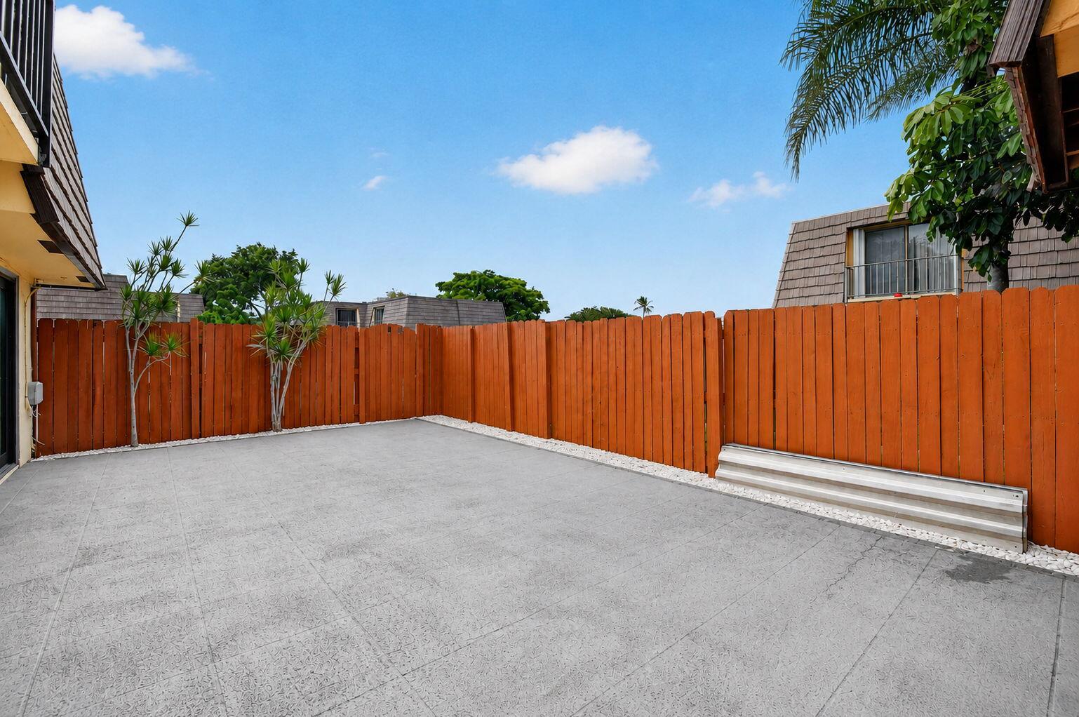 A private concrete patio enclosed by a tall orange wooden fence under a blue sky — 744 Springdale Circle, Palm Springs FL 33461, PALM SPRINGS, FL