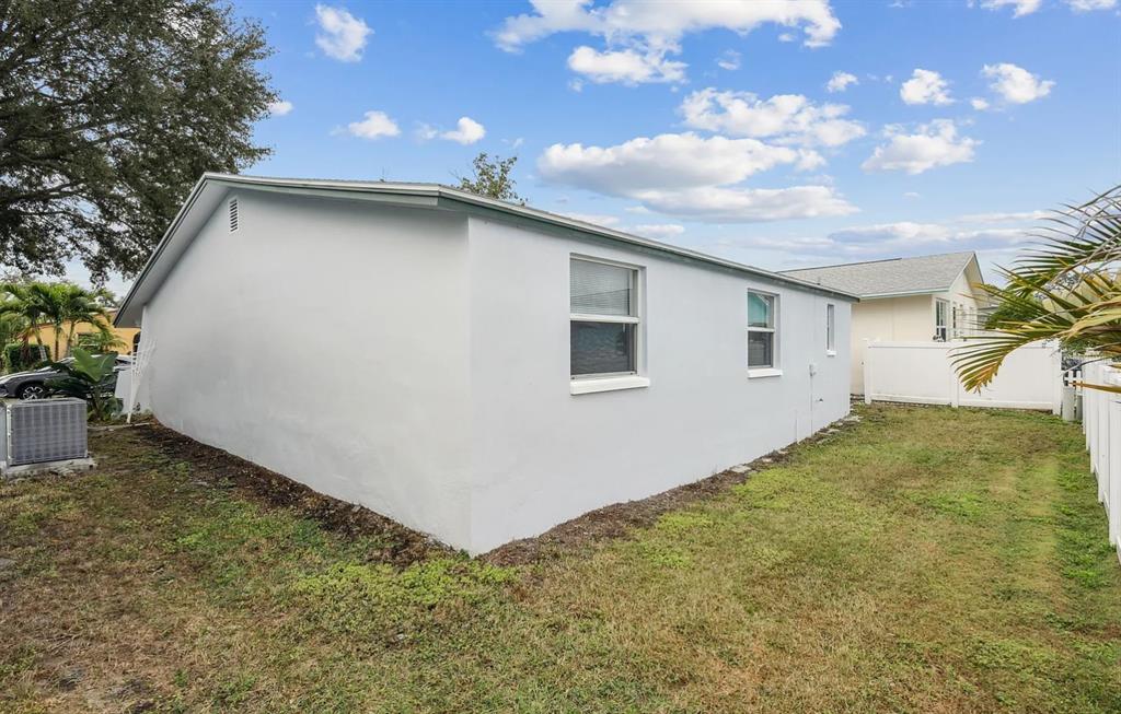 The exterior side of a white house features two windows and a grassy yard — 1018 OSPREY COURT, DUNEDIN, FL