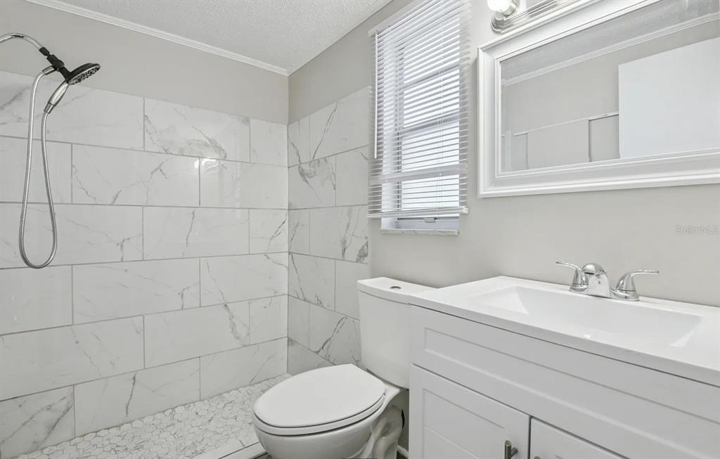 A bathroom features a marble-tiled walk-in shower, a white vanity, and a toilet — 1018 OSPREY COURT, DUNEDIN, FL
