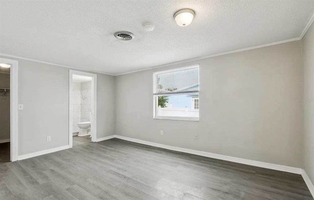 A bedroom with gray wood-look flooring, light gray walls, a window, and an attached bathroom — 1018 OSPREY COURT, DUNEDIN, FL
