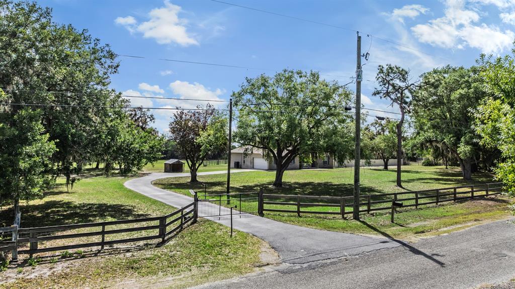 A paved driveway leads through a gated fence toward a house surrounded by large trees — 17216 ALDERMAN TURNER ROAD, WIMAUMA, FL